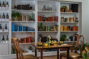 White inlaid bookshelves with books in shades of brown, blue, orange, green, and yellow next to wooden table set for breakfast