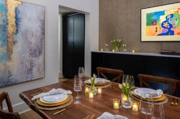 Large multipurpose room with colorful art hanging on the walls, black buffet table, and wooden table with dinner place settings and lighted candles