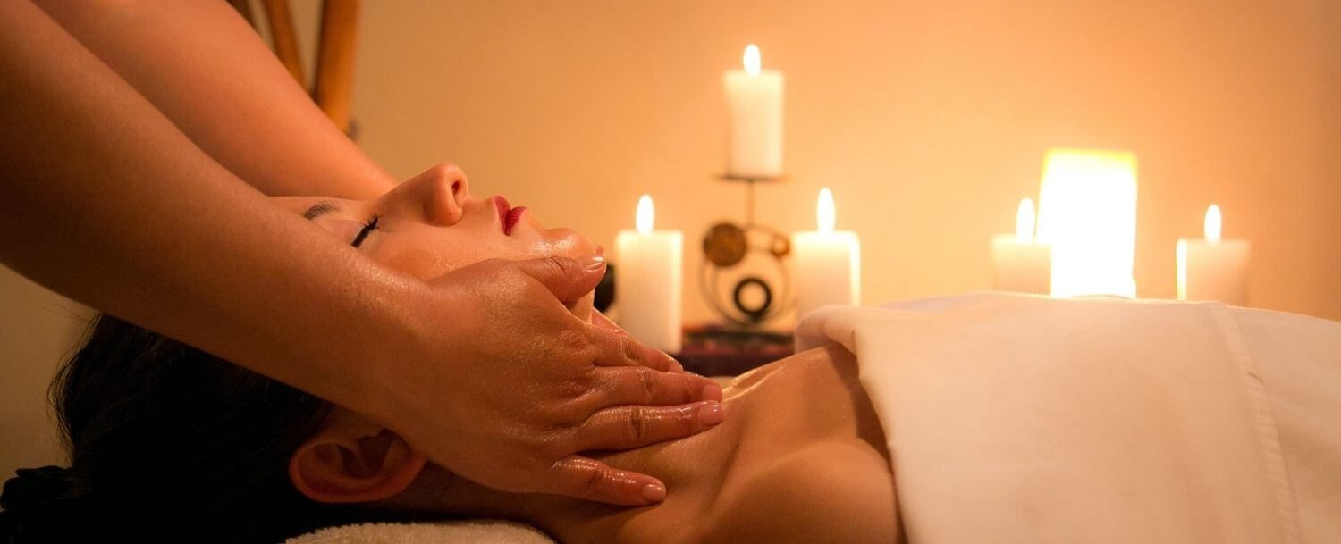 In a candlelit room, a woman is lying down getting a facial