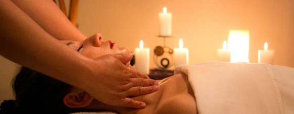 In a candlelit room, a woman is lying down getting a facial