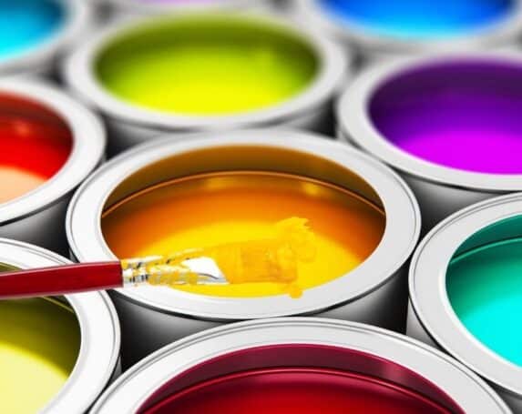 open cans of multi-colored paint with paintbrush sitting on top dripping yellow paint