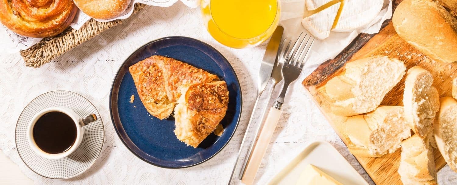 cup of coffee, glass of orange juice, plate with pastry and trays of pastries