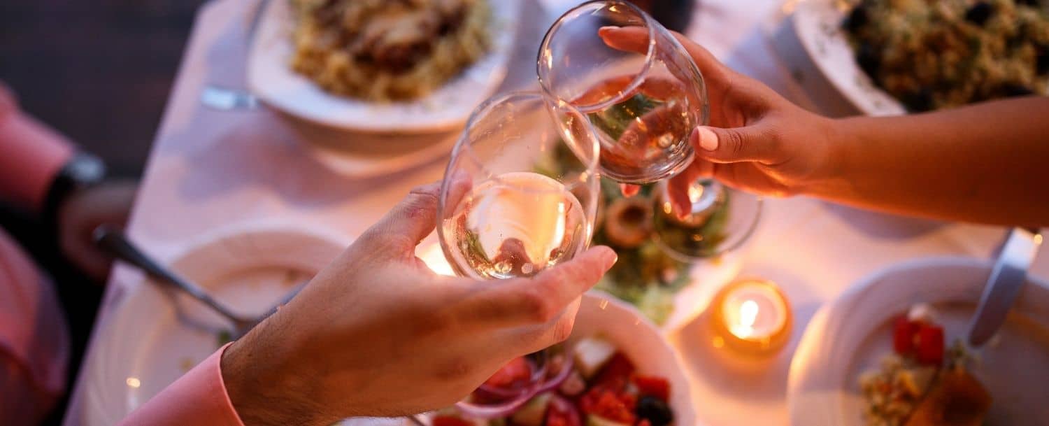 couple clinking glasses of white wine while eating dinner