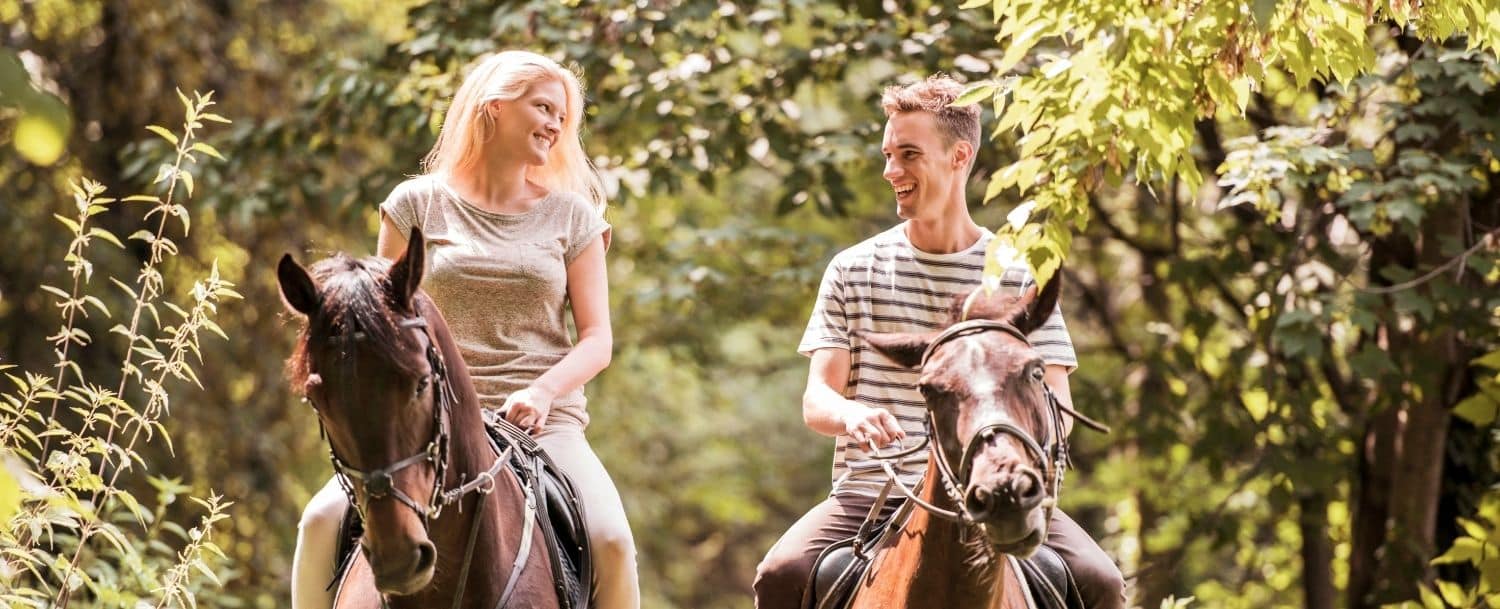 a man and a woman horseback riding in the woods
