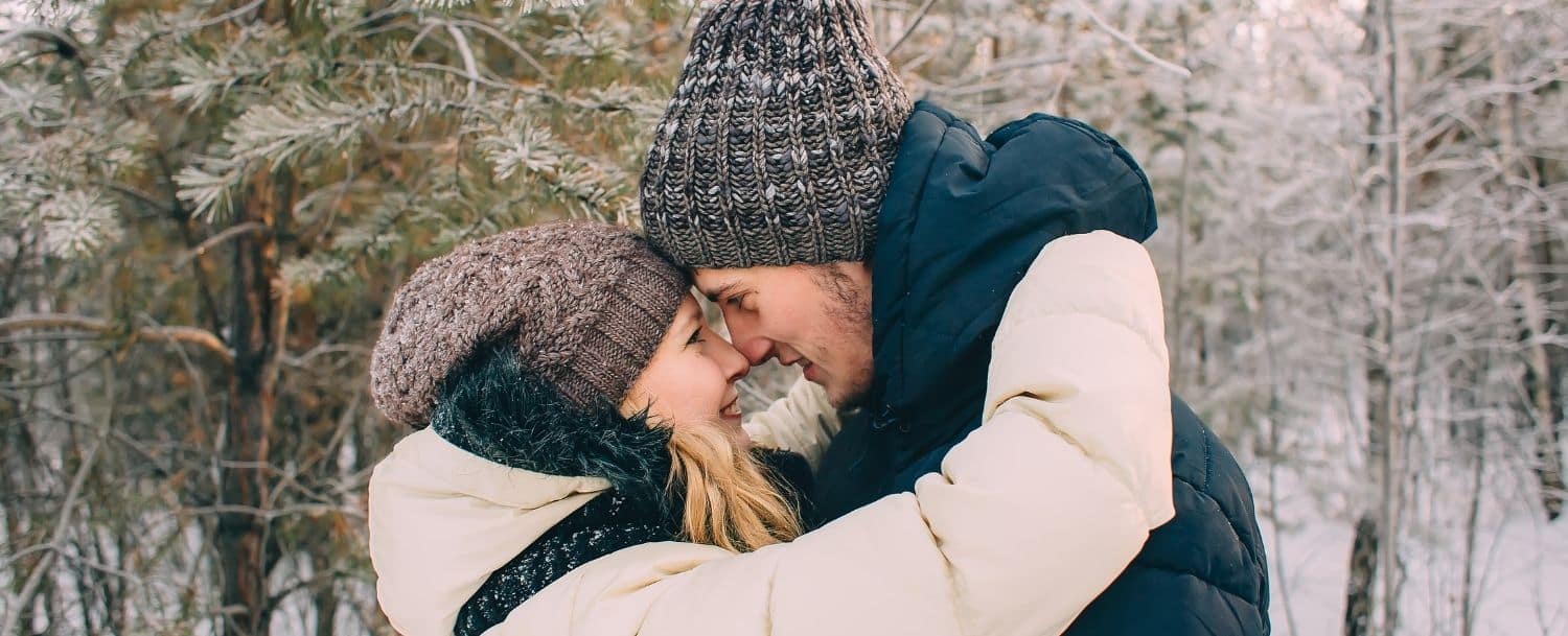 young couple snuggling face to face while hiking in the winter