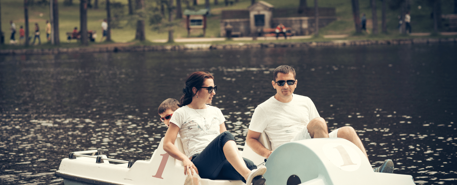 family of three wearing sunglasses enjoying a ride on a white pedal boat 