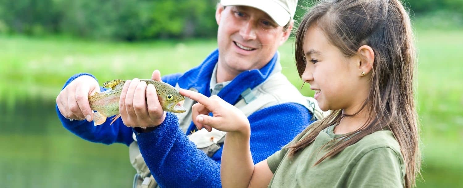 father showing daughter a fish while fly fishing