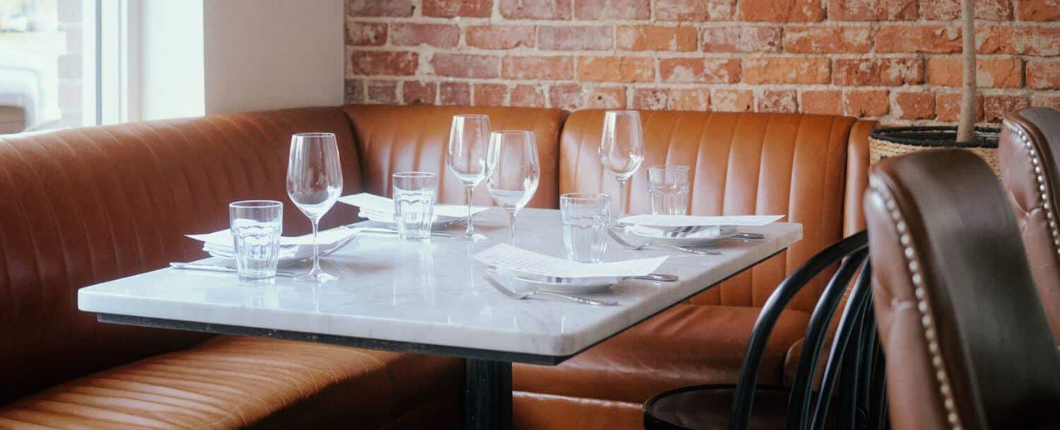 booth by main street window with comfy leather seating and a table set for four at kindred