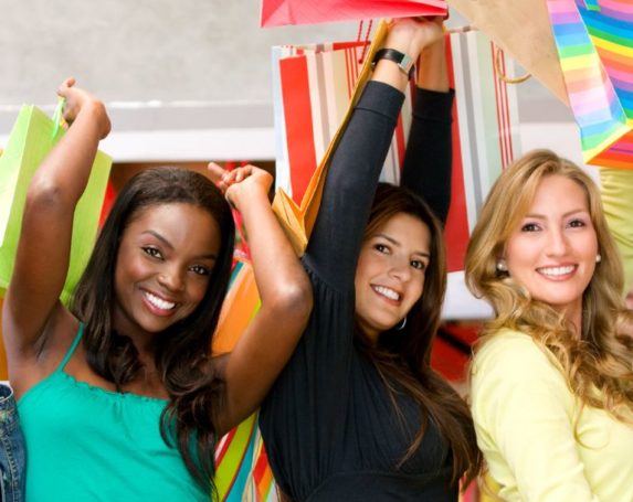 5 ladies smiling and holding shopping bags high over their heads.