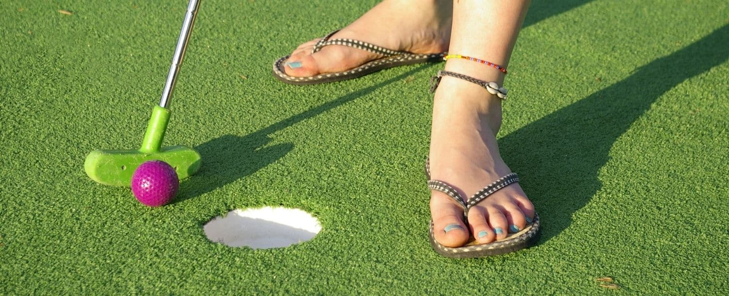 closeup of mini golf hole with woman's feet in flip flops