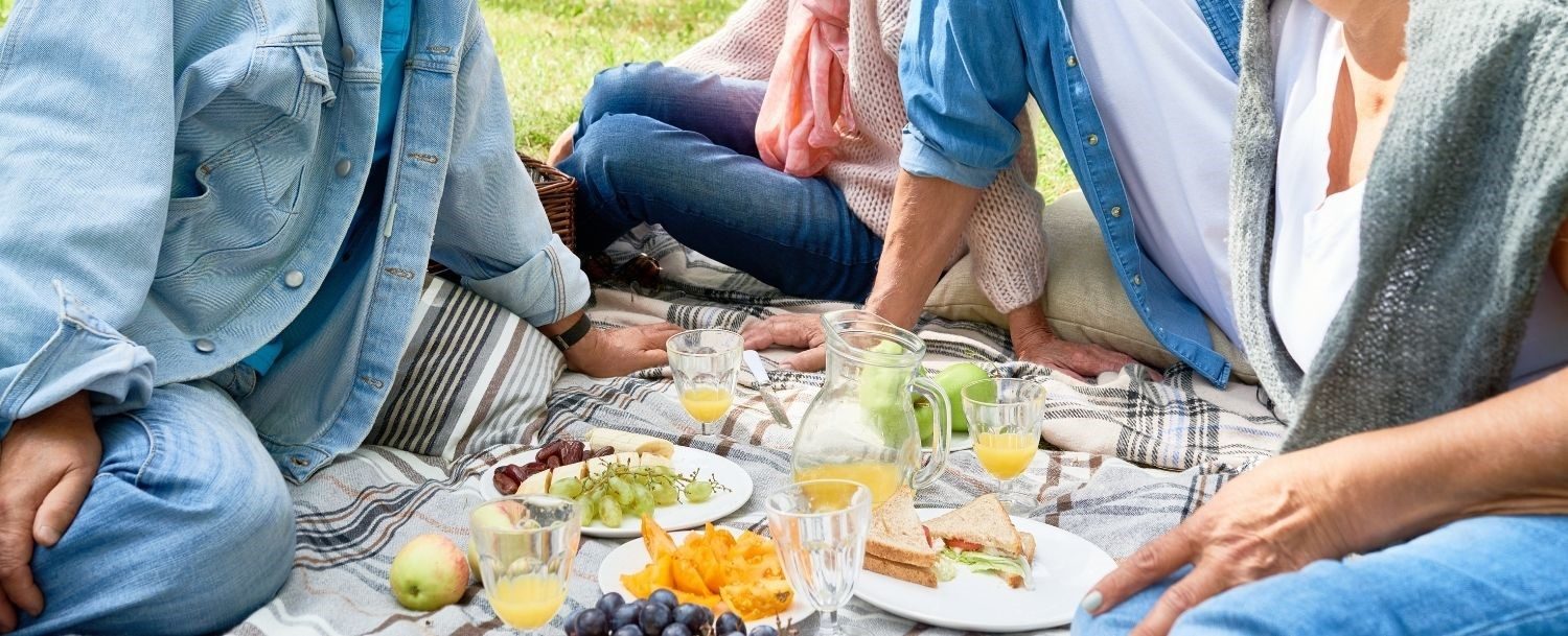 Four people sitting on the lawn enjoying a picnic lunch spread out on a blanket