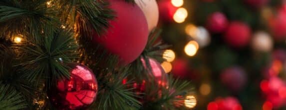 closeup of red christmas ornaments on evergreen with blurred lights in background