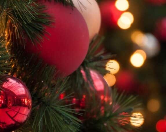 closeup of red christmas ornaments on evergreen with blurred lights in background