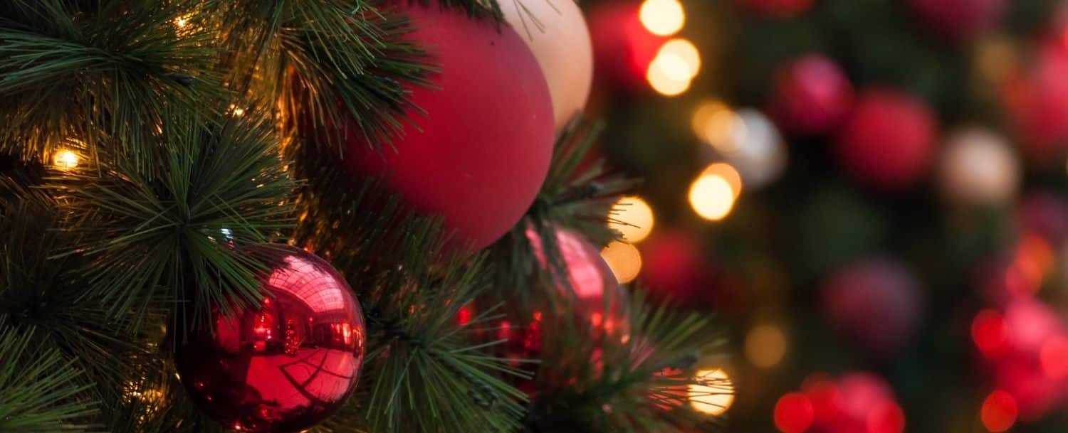 closeup of red christmas ornaments on evergreen with blurred lights in background