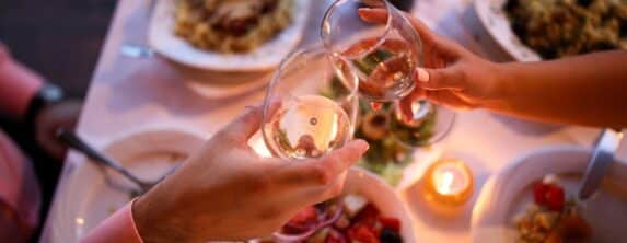 view looking down on a couples hands holding glasses of wine as they toast over a romantic dinner