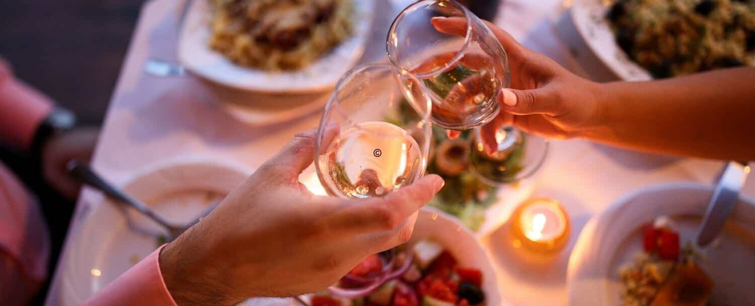 view looking down on a couples hands holding glasses of wine as they toast over a romantic dinner