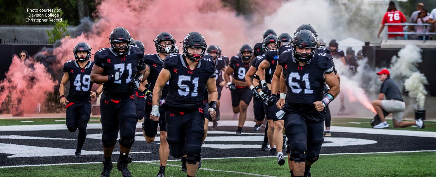 Davidson College football players running onto the field through smoke before a home game.