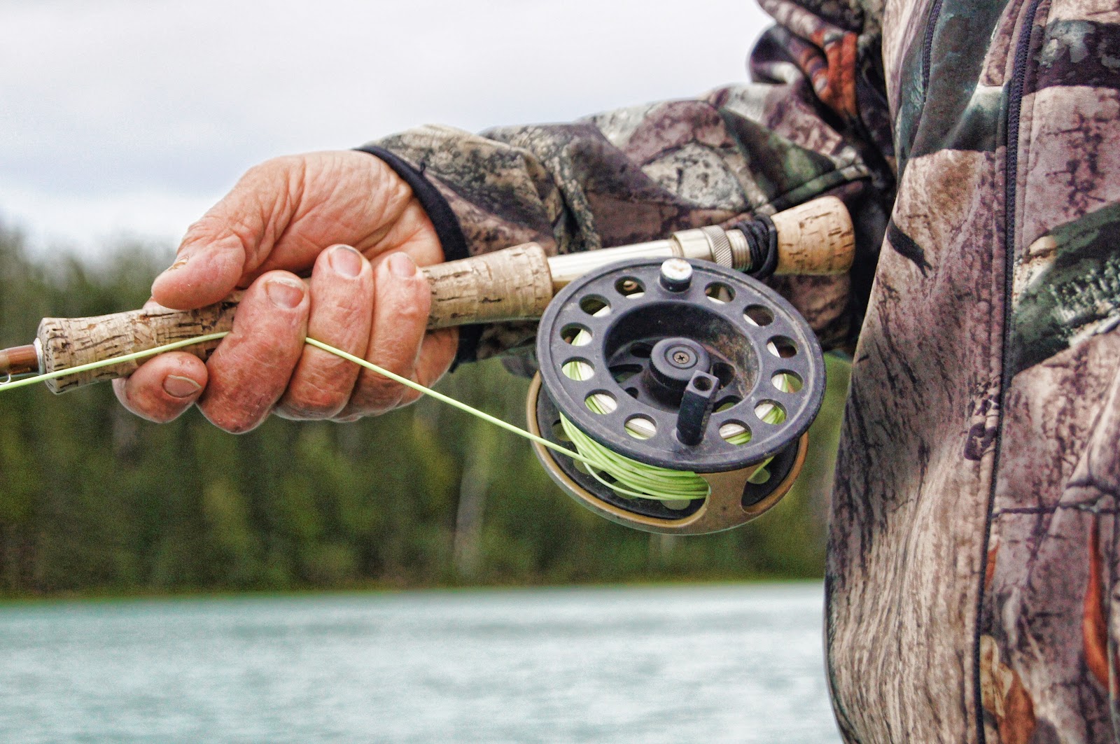 Man holding a fishing rod against a backdrop of trees and a lake