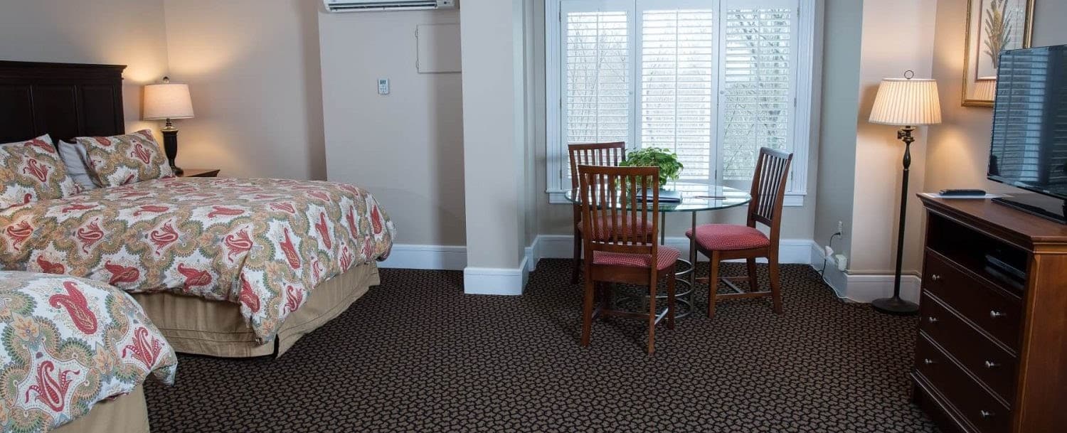 Guest room at Davidson Village Inn with two beds, table and three chairs, dresser and TV, and large window