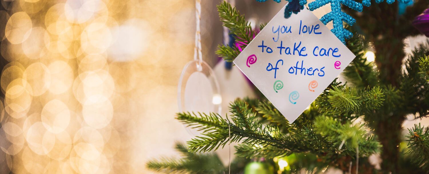 Closeup of Christmas tree branch with diamond-shaped tag saying, “you love to take care of others.”