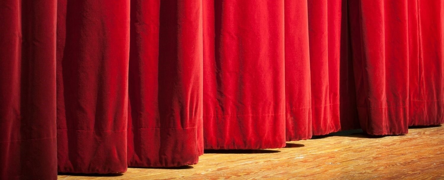 Front of a theatre stage with closed red velvet curtains