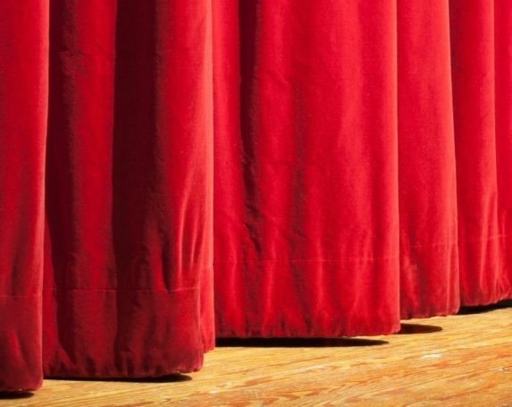 Front of a theatre stage with closed red velvet curtains
