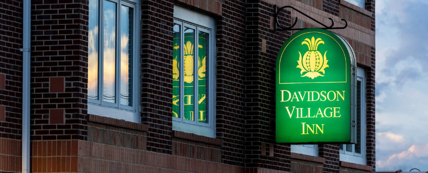 Red brick building housing Davidson Village Inn at night with lit green and yellow sign reflecting in window
