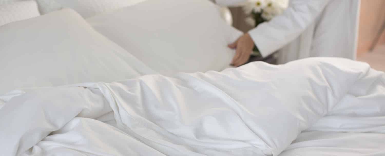 Person with white robe making bed with white sheets