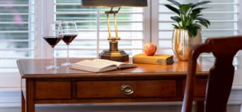 Close up view of oak desk with drawer and lamp with red wine glasses, plant and books on top
