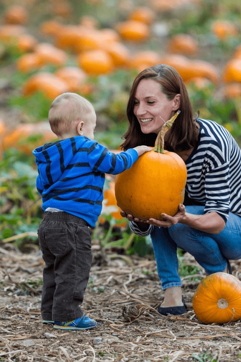Mother and son smiling as they pick a pumpkin.