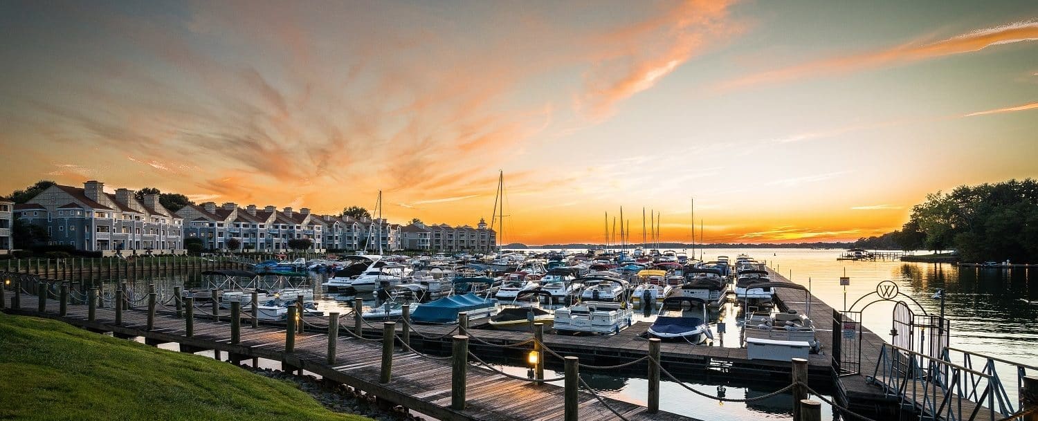 Large marina filled with boats near large body of water with sun setting in the background